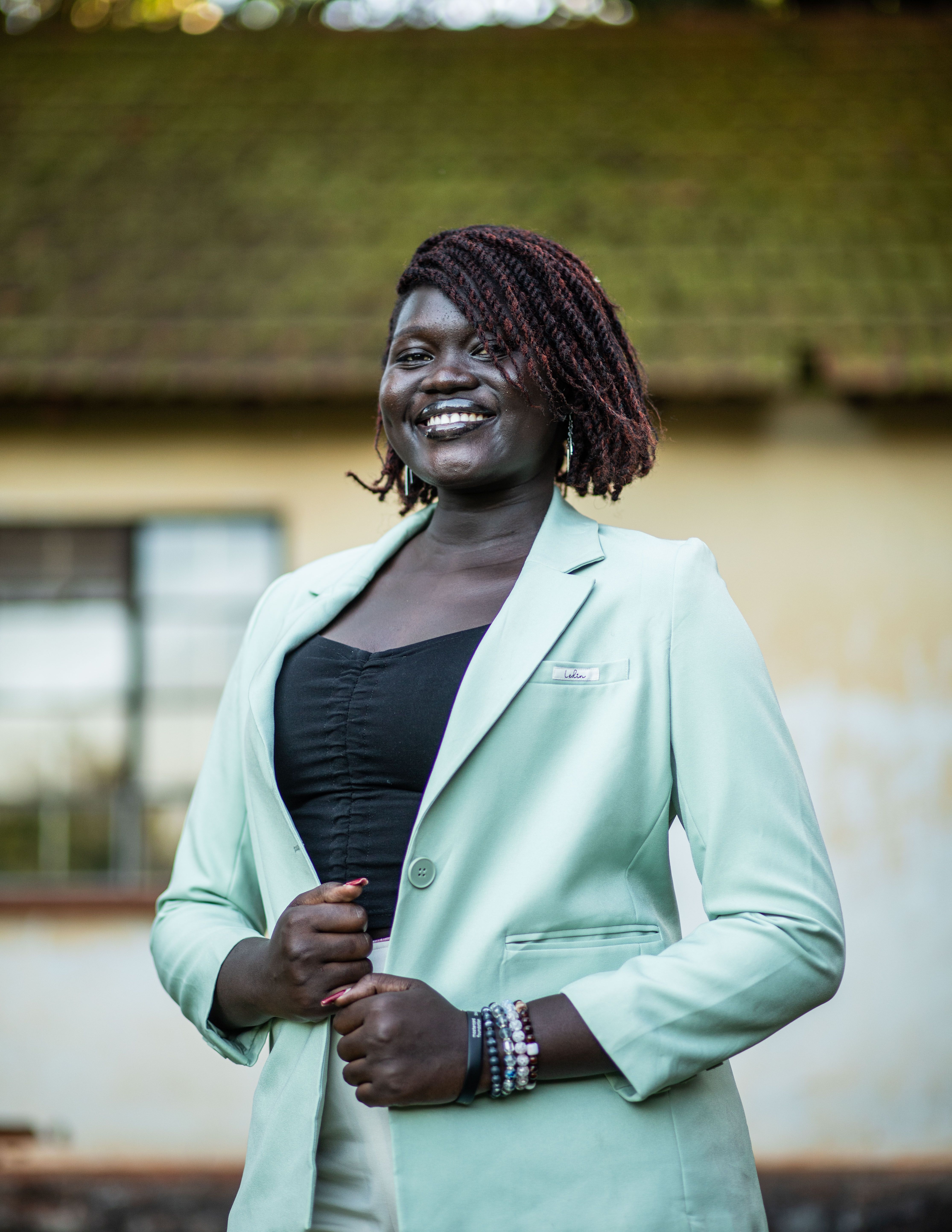 A smiling woman in a mint blazer poses confidently outside a rustic building.