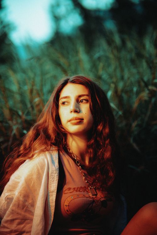 Free Portrait of a young woman with long hair, outdoors in natural light, surrounded by greenery. Stock Photo