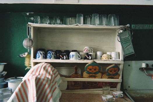 Cozy vintage kitchen shelf featuring glasses, mugs, and rustic decor.