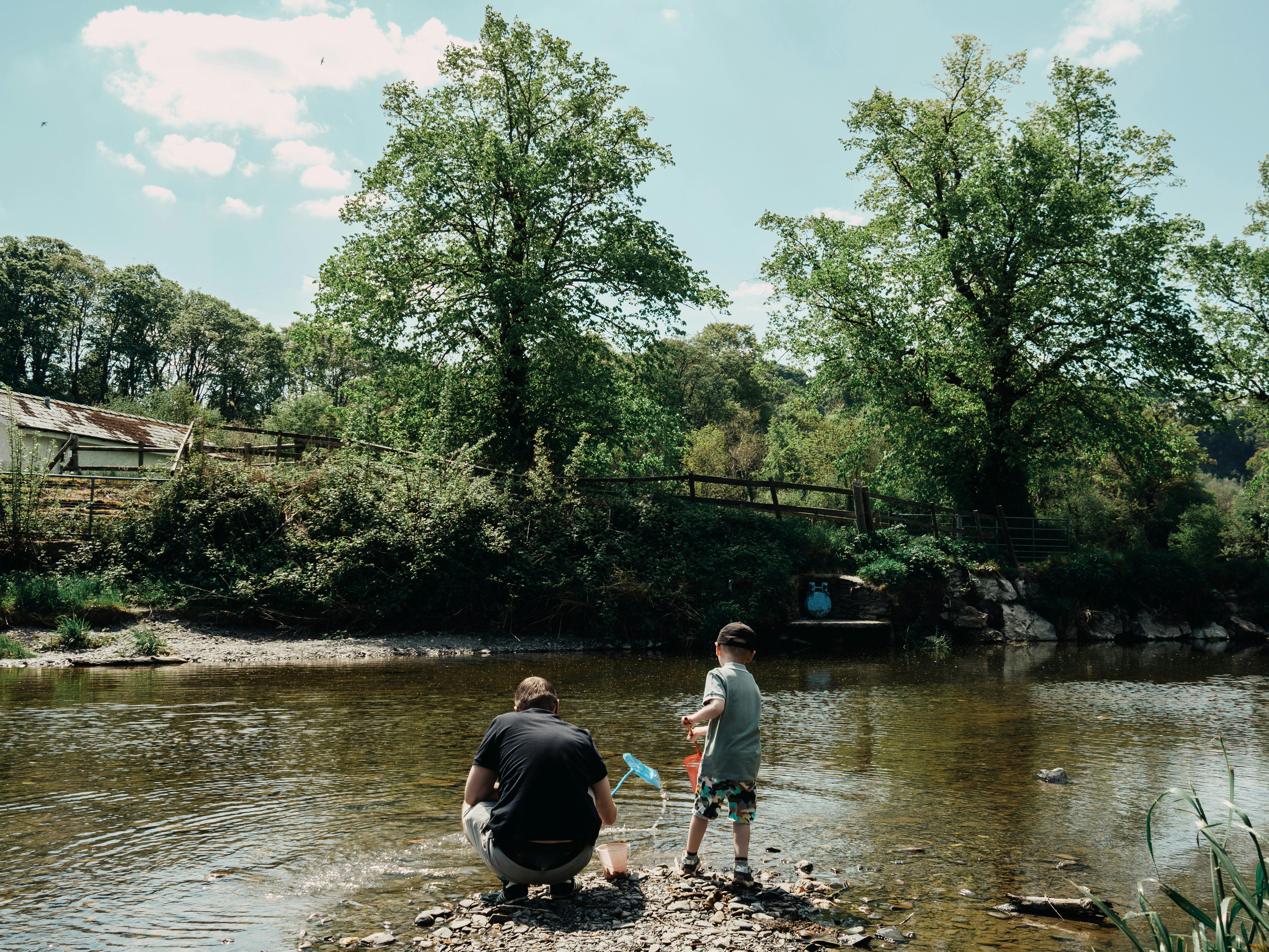 A serene scene of a father and son bonding by a stream in Llanfair Talhaiarn, Wales.