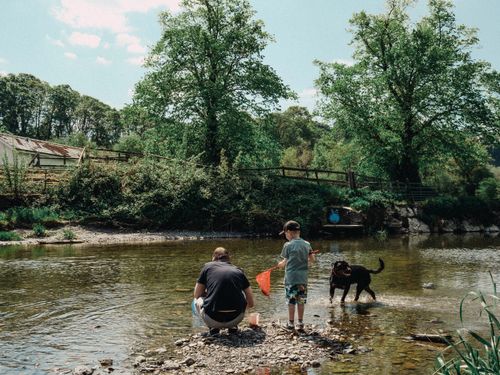 Free A father and son enjoying a fishing day by a serene river in Llanfair Talhaiarn, Wales, with their dog. Stock Photo