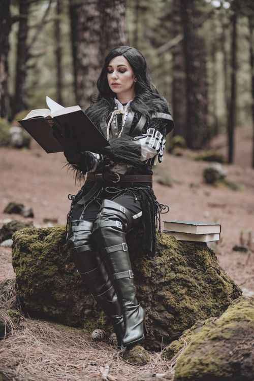 Free A woman in detailed cosplay reads a book while sitting in a mystical forest. Stock Photo