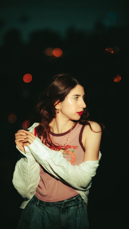 Free Stylish young woman posing under night lights with urban bokeh. Stock Photo