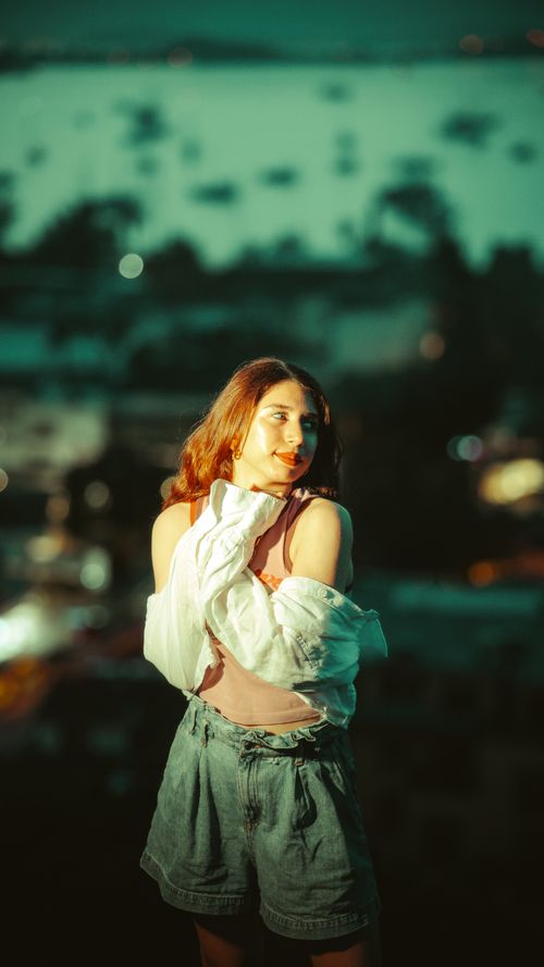 Free Serene portrait of a young woman at dusk with a captivating blurred cityscape backdrop. Stock Photo