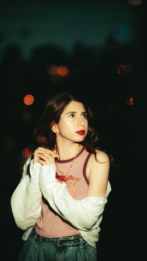 Free Elegant portrait of a young woman in stylish attire captured at night with city lights in the background. Stock Photo