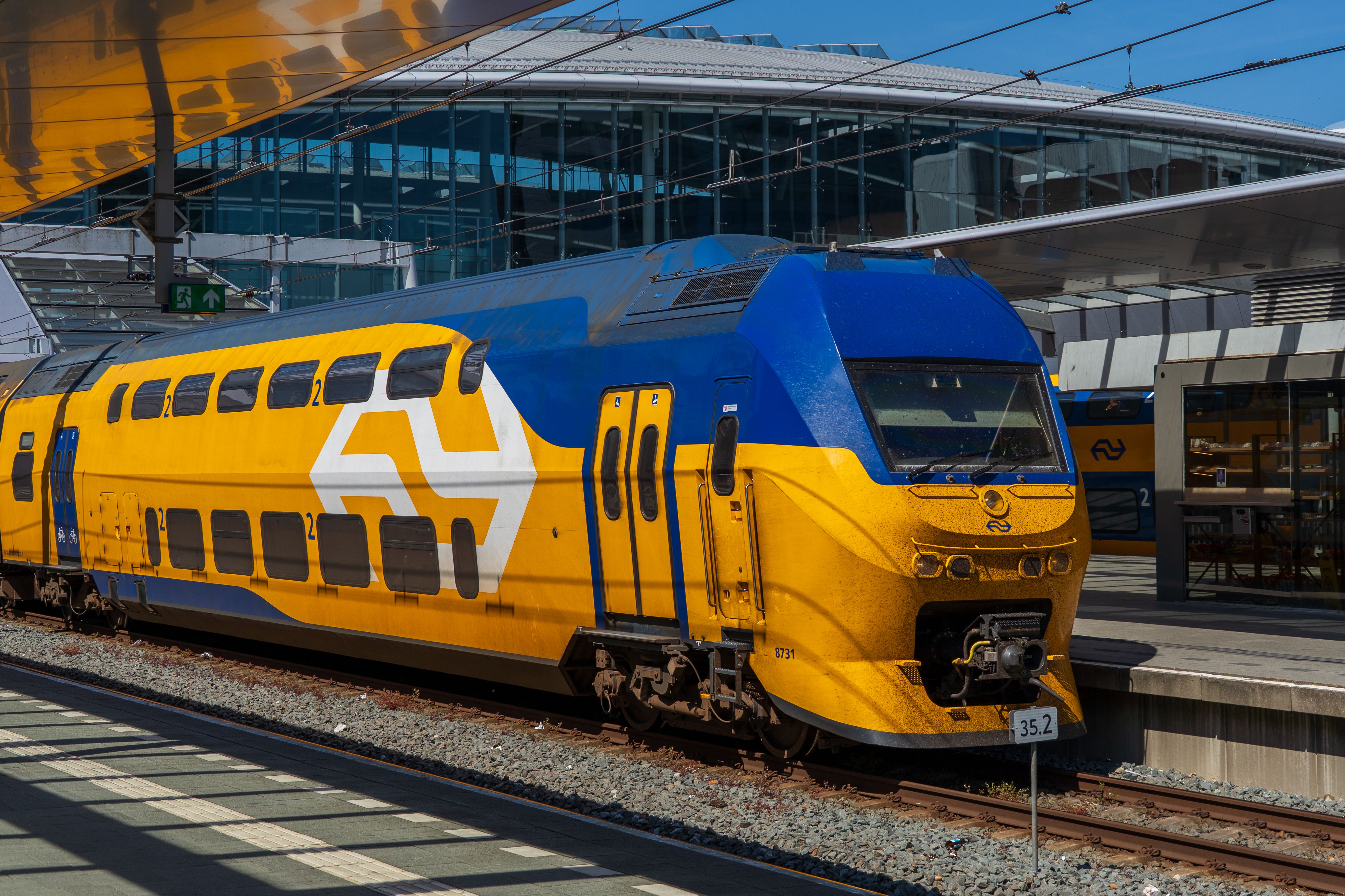 A bright blue and yellow intercity train at a contemporary railway station on a sunny day.