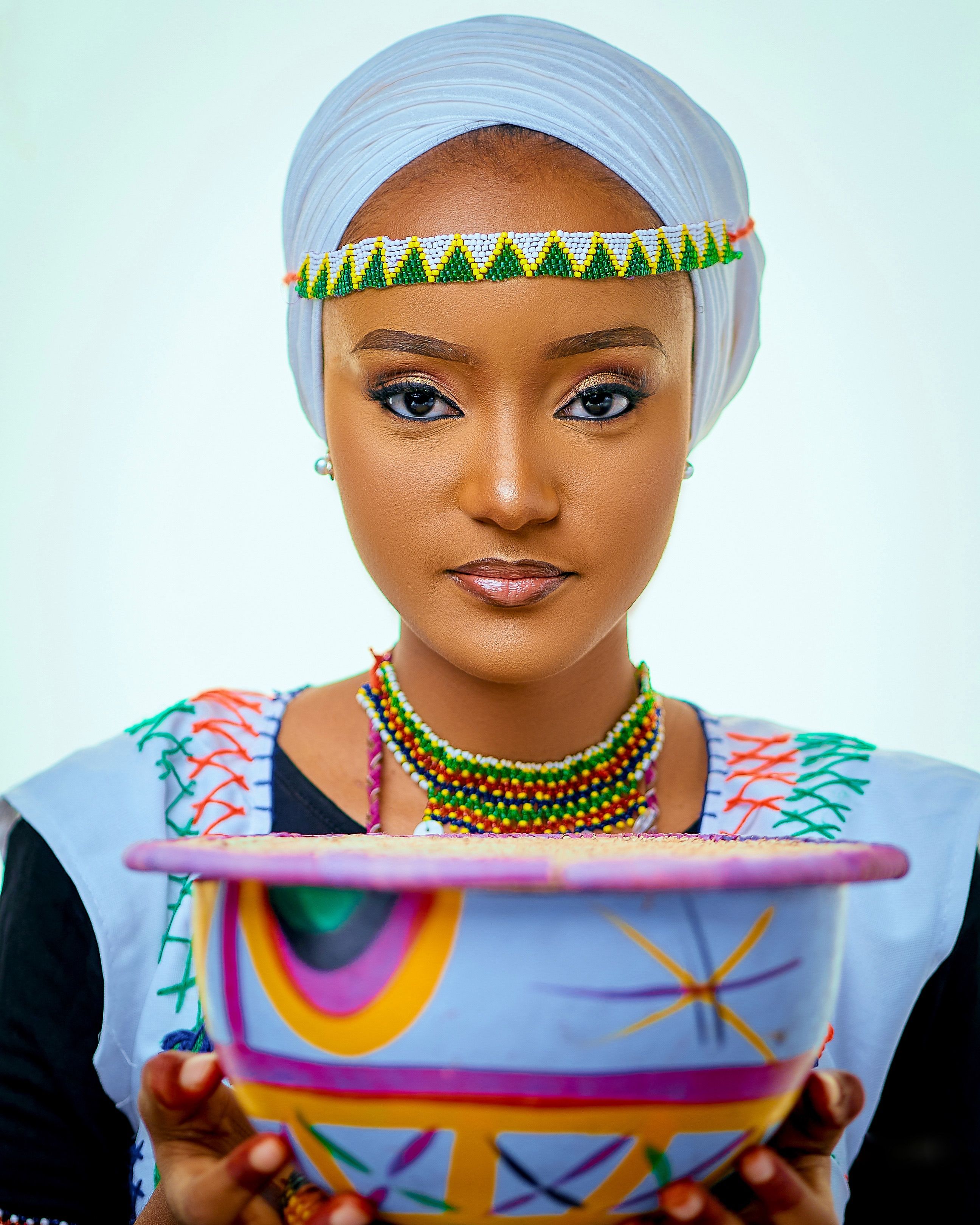 A woman in colorful traditional attire holding a decorative bowl.