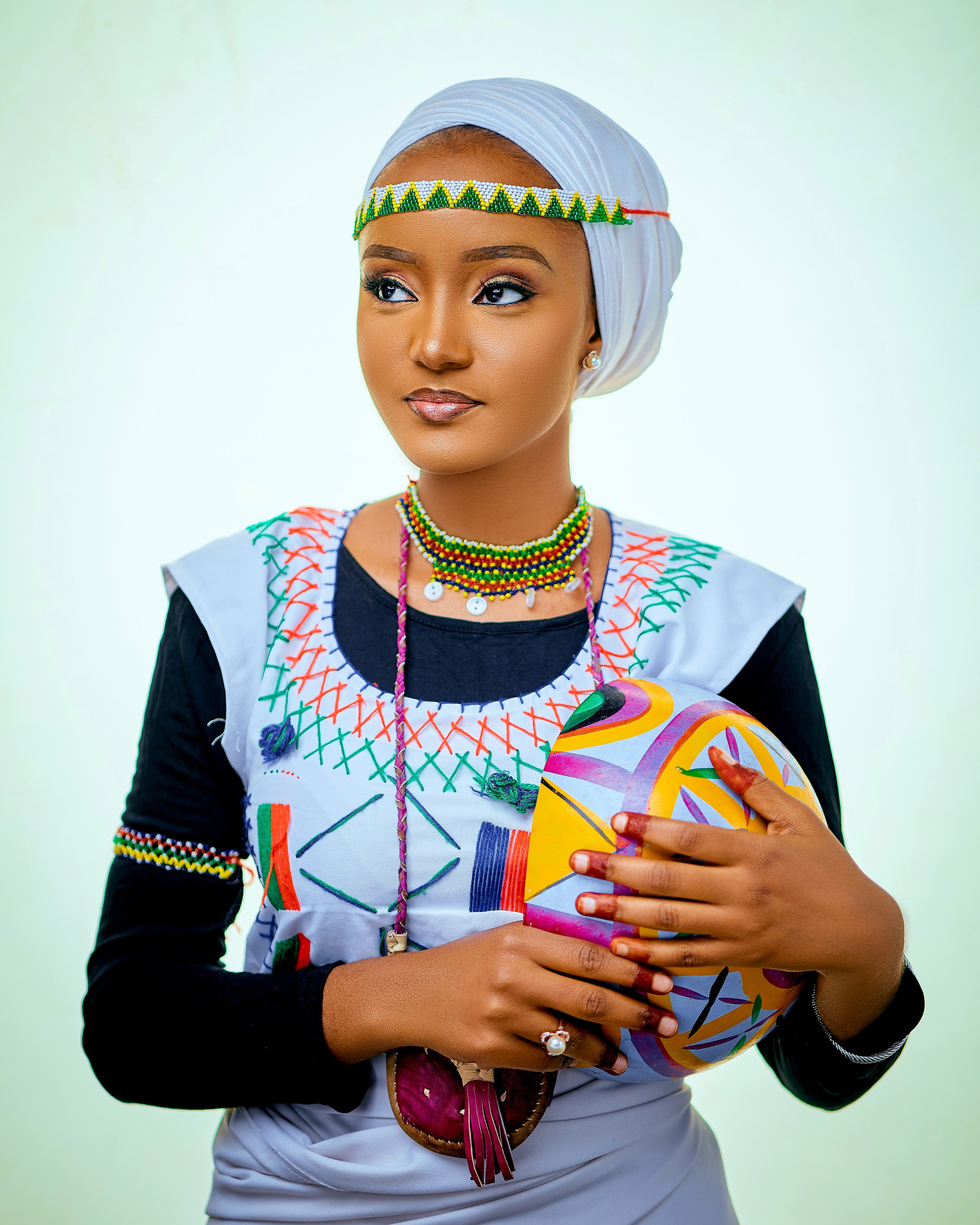Elegant woman in colorful African clothing and jewelry holding a painted gourd.