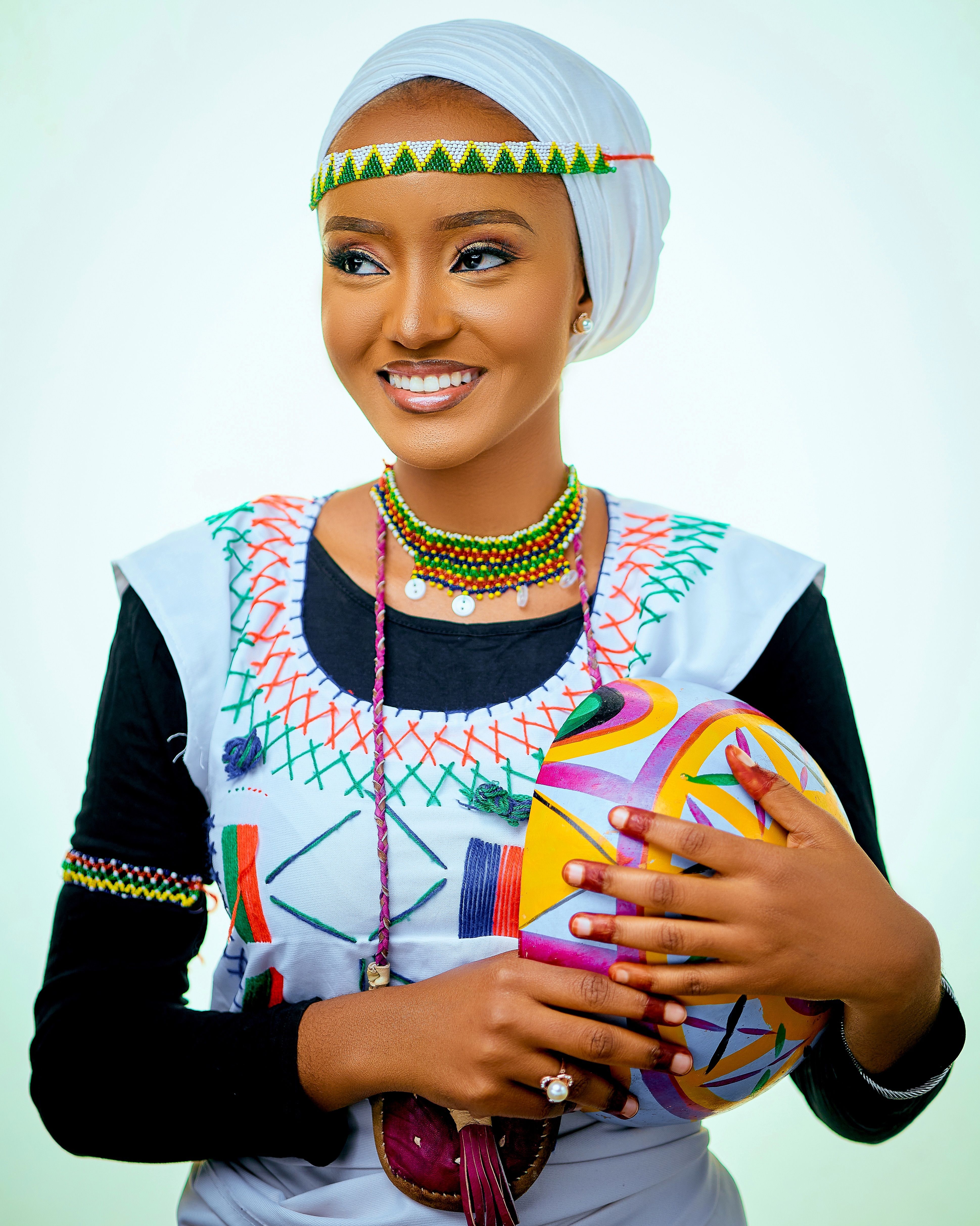 Smiling woman in vibrant traditional attire holding a decorated calabash.