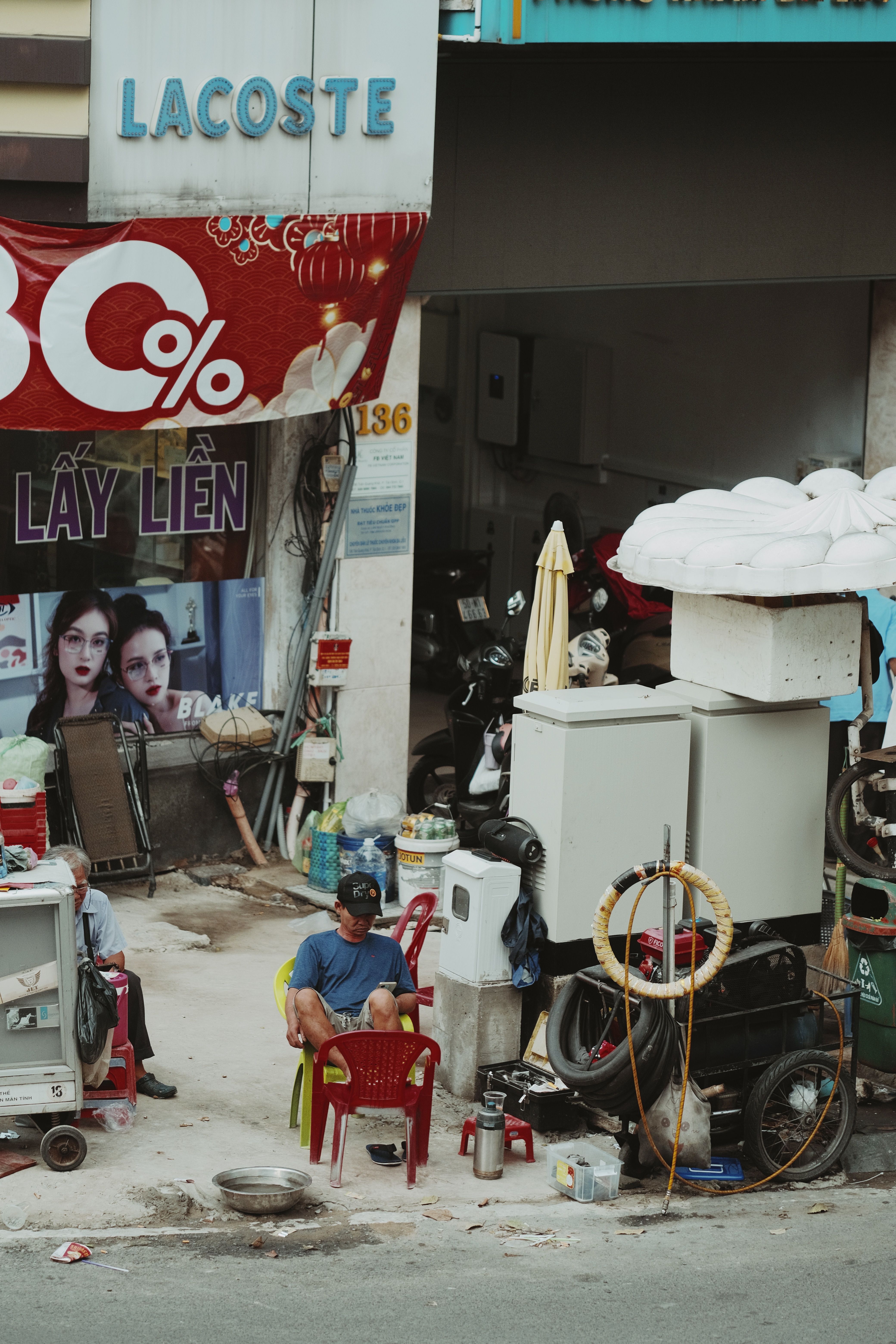 Urban street scene showing people sitting under a discount banner with industrial equipment.