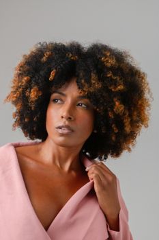 Stylish portrait of a woman with curly hair wearing a pink outfit against a neutral background.