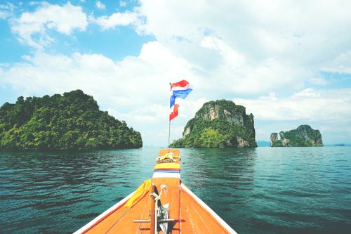 Free Long-tail boat sailing towards lush islands in the Andaman Sea on a sunny day. Stock Photo