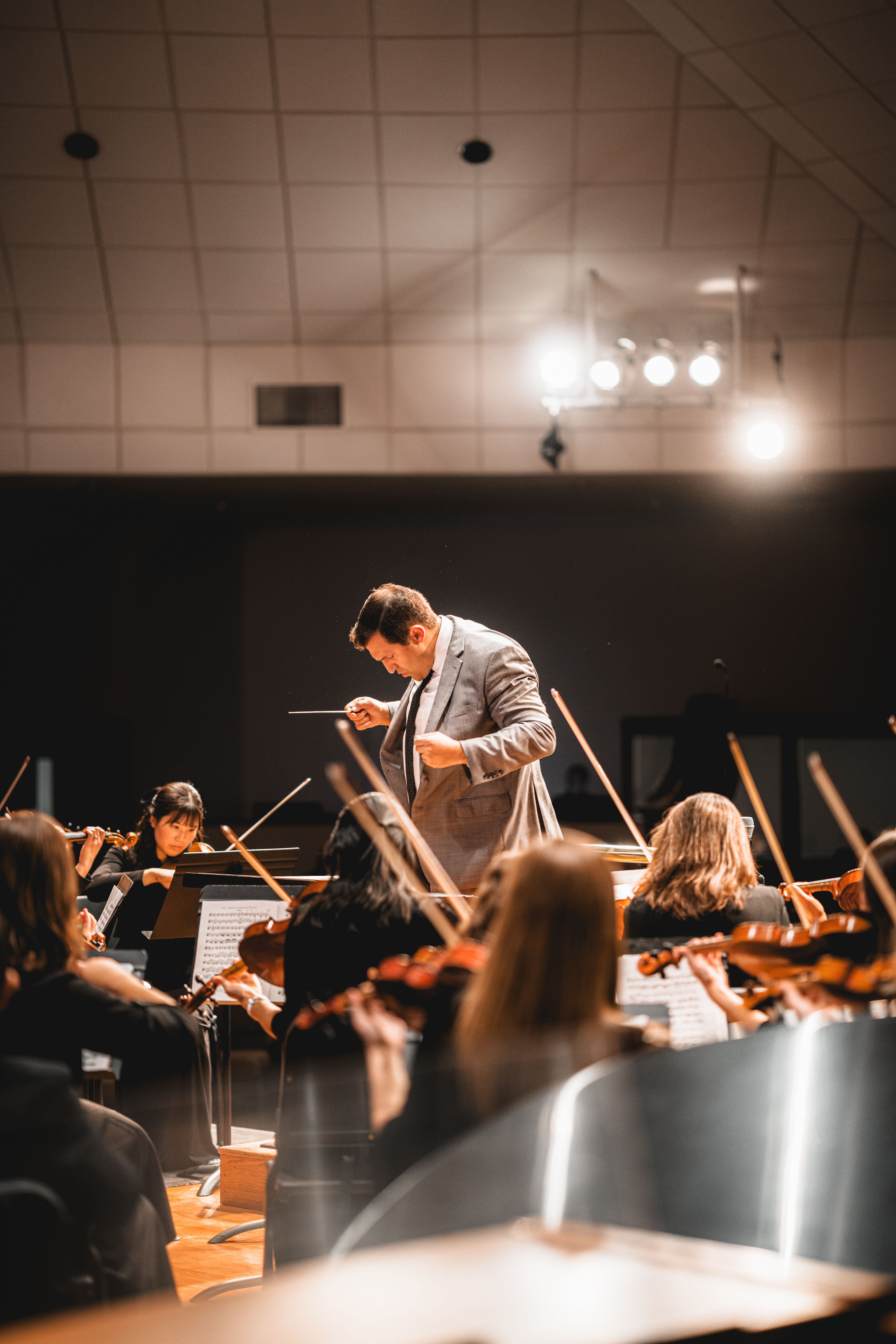 A conductor skillfully leads an orchestra with string instruments under dramatic lighting.