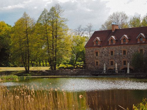 Free Picturesque stone house by a serene pond with lush greenery, capturing the essence of a spring day. Stock Photo