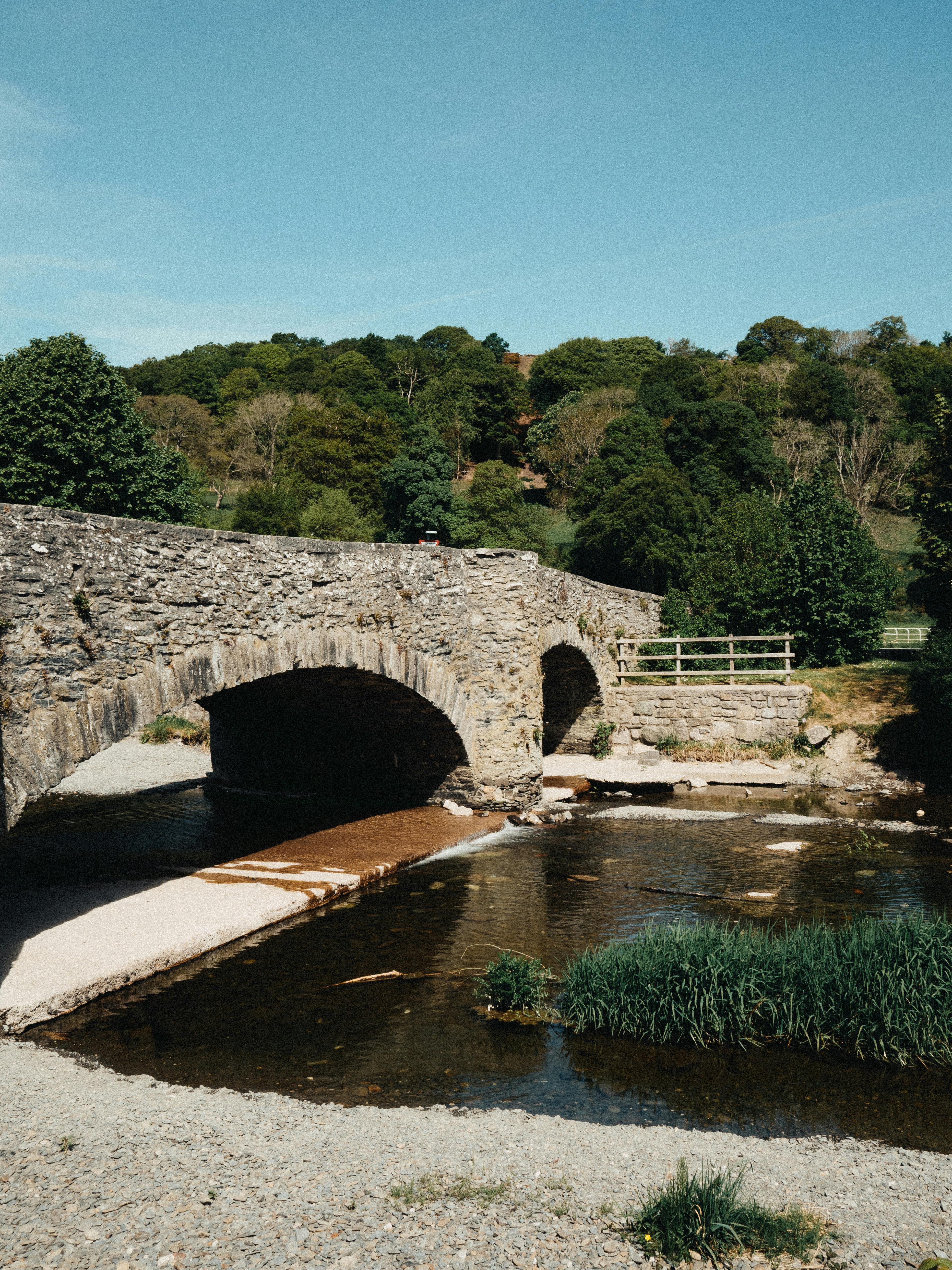 Historic stone bridge over a serene river in the village of Llanfair Talhaiarn, Wales.