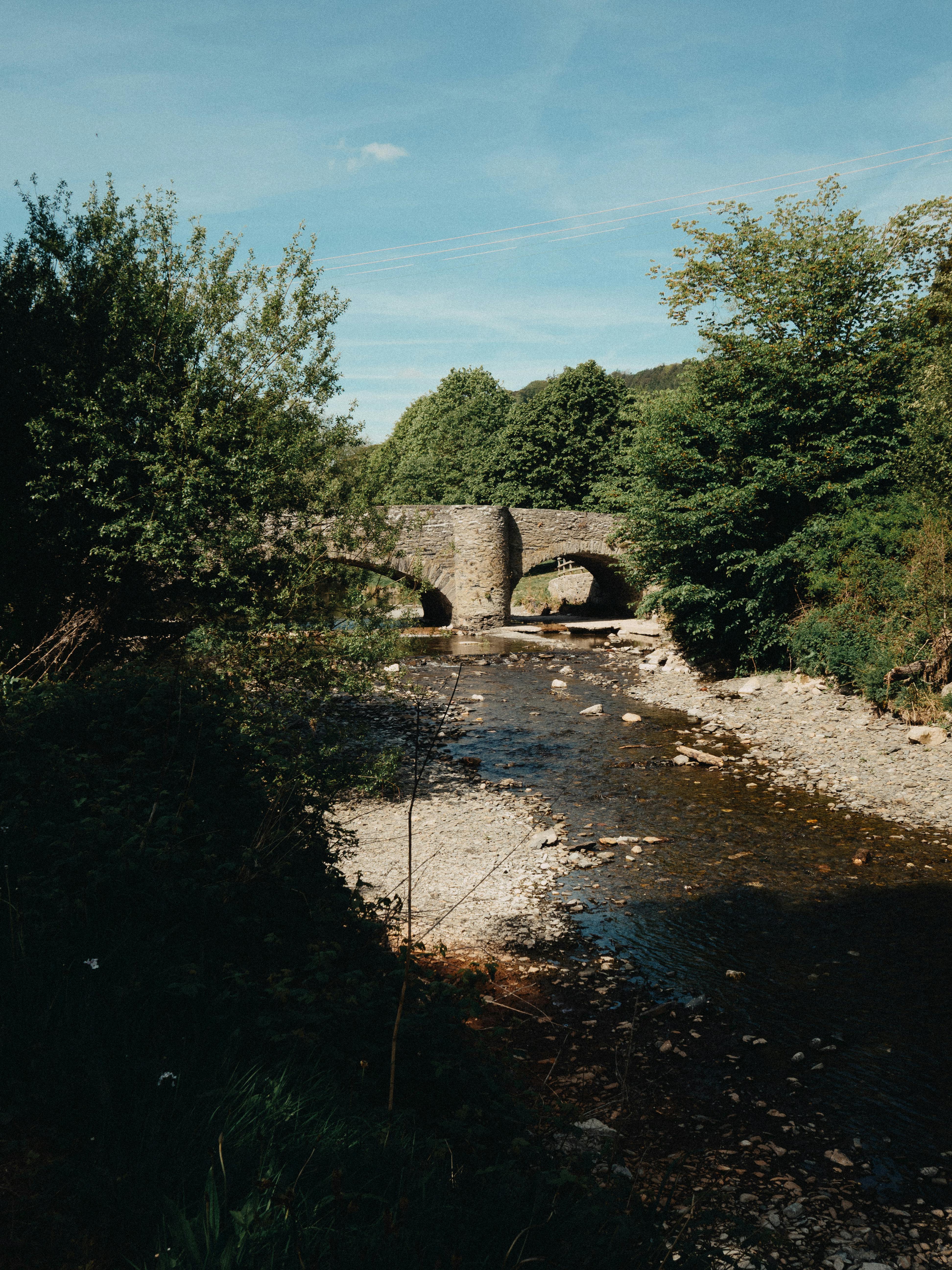A tranquil scene of a stone bridge over a river surrounded by lush greenery in Llanfair Talhaiarn, Wales.