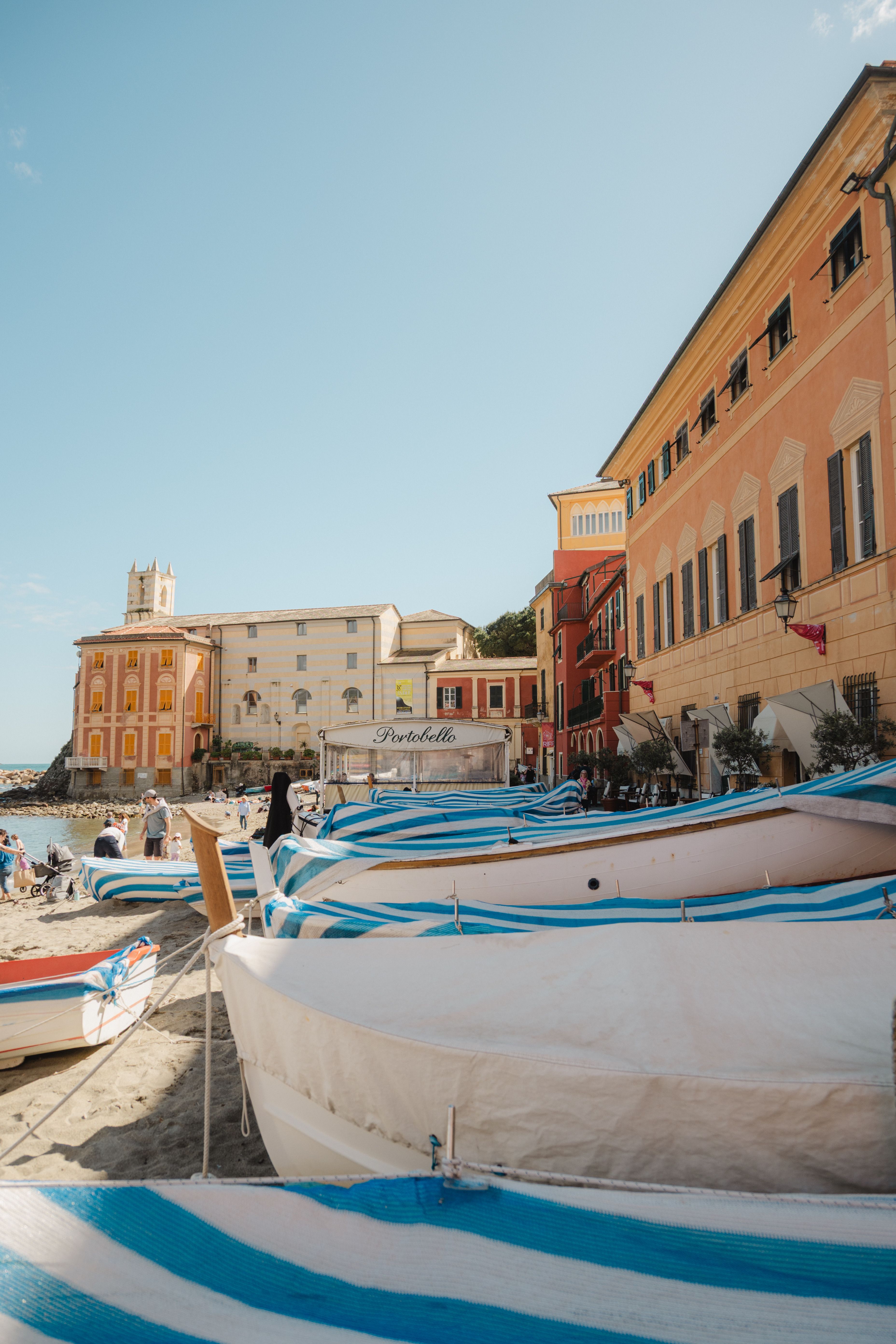 Vibrant striped boats by historic architecture in a sunny Italian beachfront.