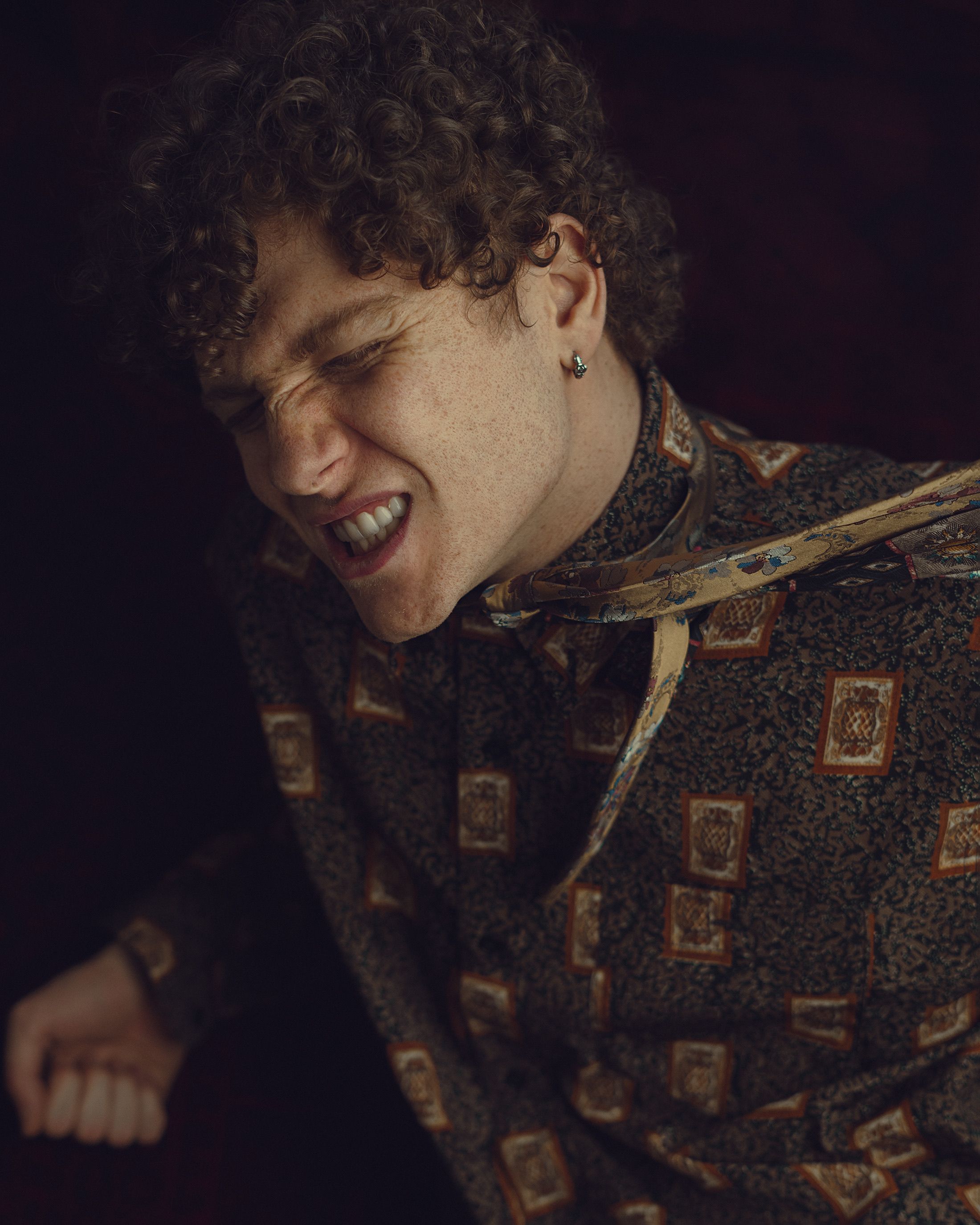 Curly-haired young man with intense expression, indoors, artistic fashion.