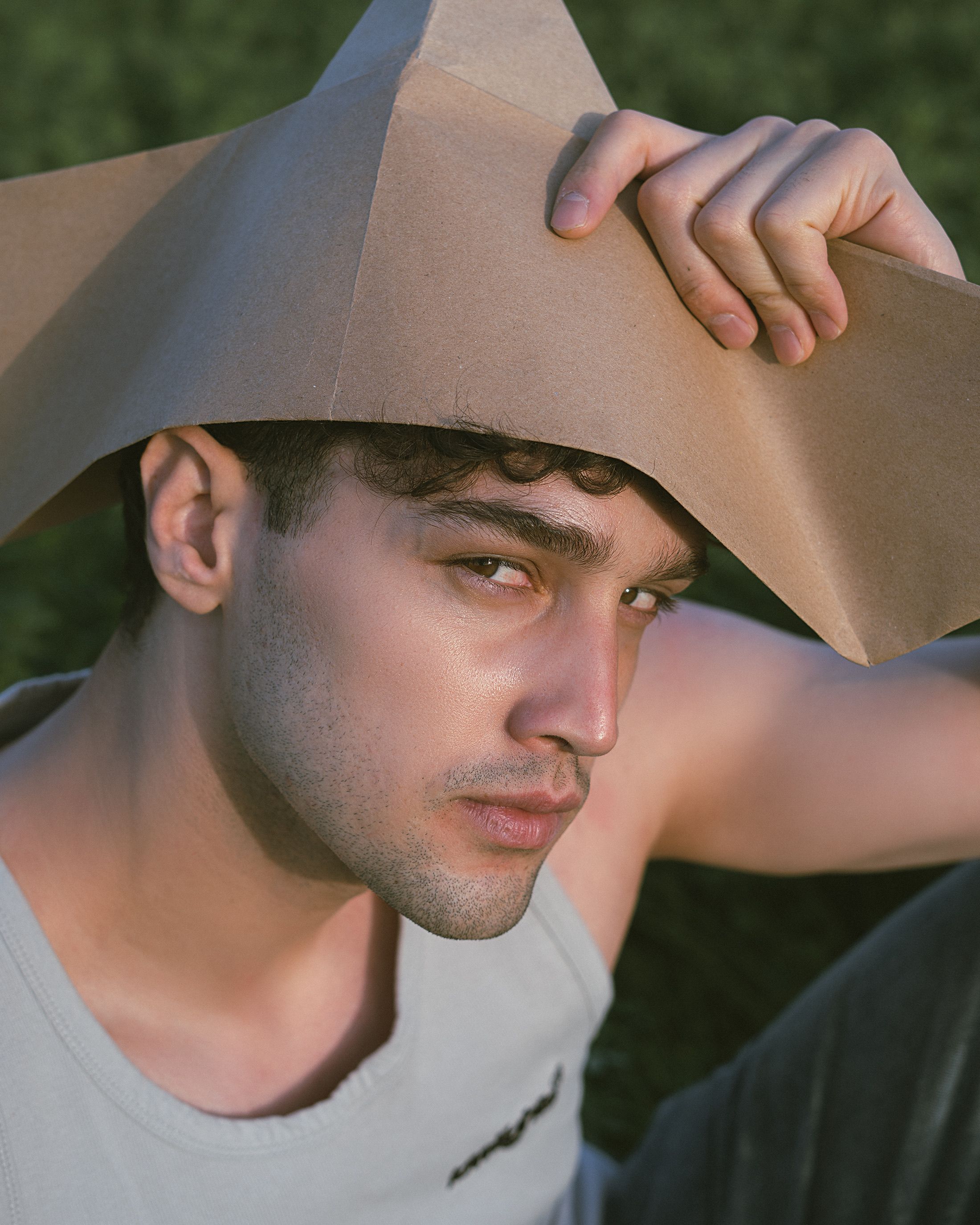 A young man with a paper hat poses outdoors, basking in the sunlight.