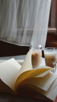 Open book and coffee by a sunlit window, offering a peaceful reading nook ambiance.