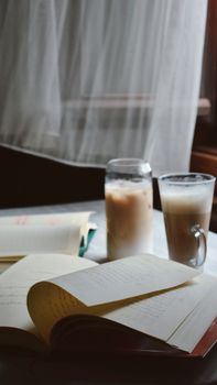 A warm indoor scene featuring coffee and open books on a table by a window.