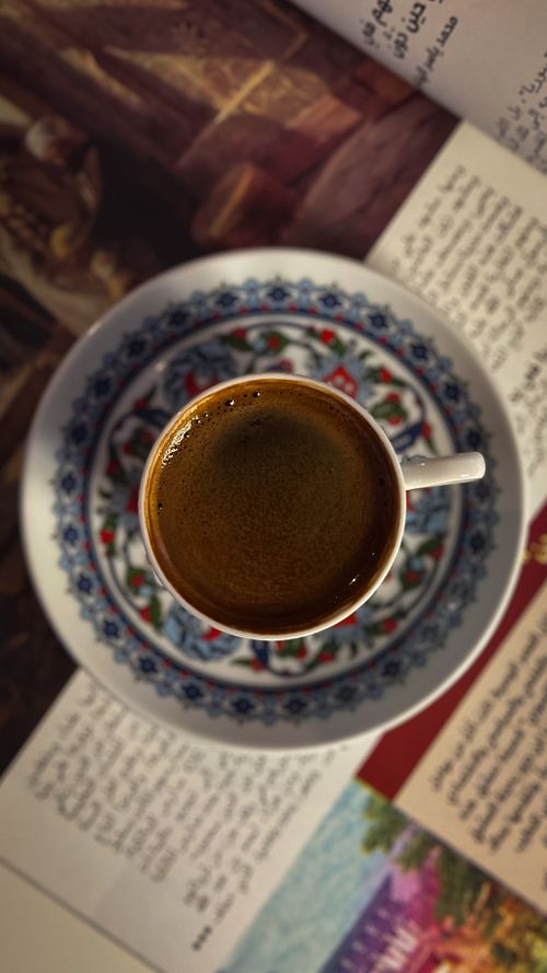 Free Turkish coffee in an ornate cup and saucer on a table with open books. Stock Photo