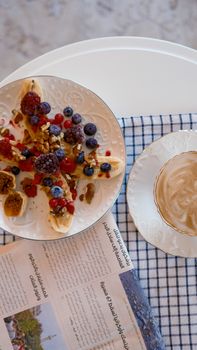 Flat lay of a nutritious breakfast with berries, nuts, and coffee on a white table.