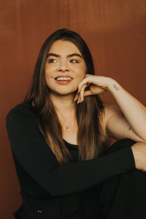 Free Relaxed portrait of a smiling woman sitting against a brown backdrop. Stock Photo