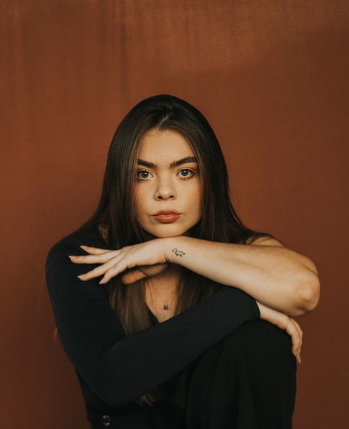 Free A woman poses with her arms crossed in an artistic portrait against a brown backdrop. Stock Photo