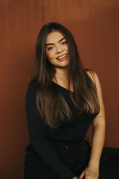Free A woman with long hair smiling warmly seated against a brown backdrop. Stock Photo