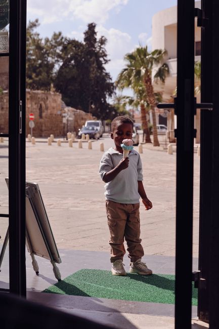 Young boy savoring an ice cream cone outside a shop on a sunny day.