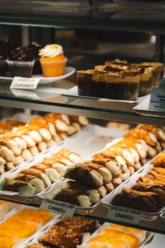 A variety of Italian pastries including cannoli and cupcakes in a bakery display case.