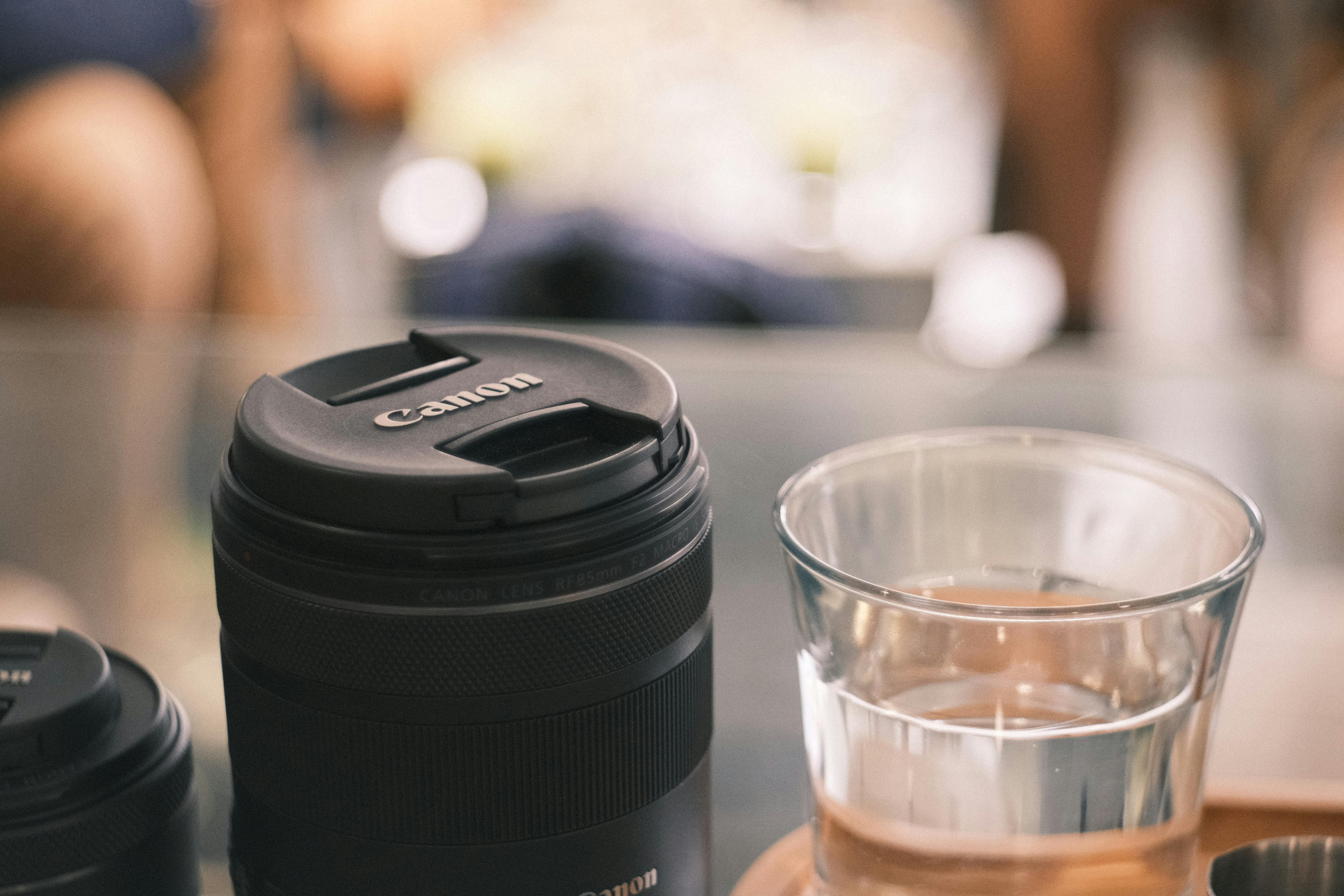 Photograph of a camera lens next to a glass of water on a table.