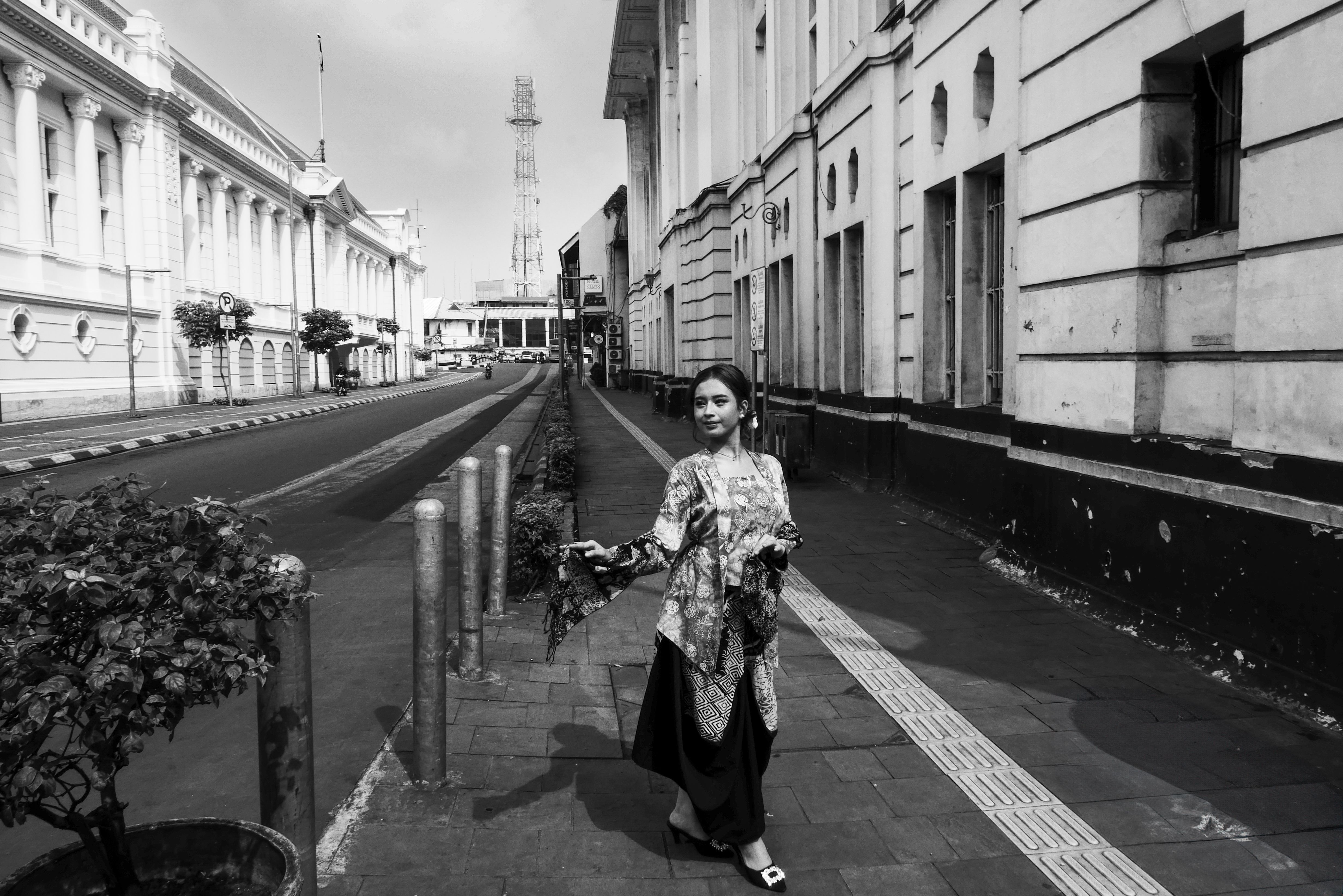 A woman in traditional attire walks on a historical street in Jakarta, Indonesia.