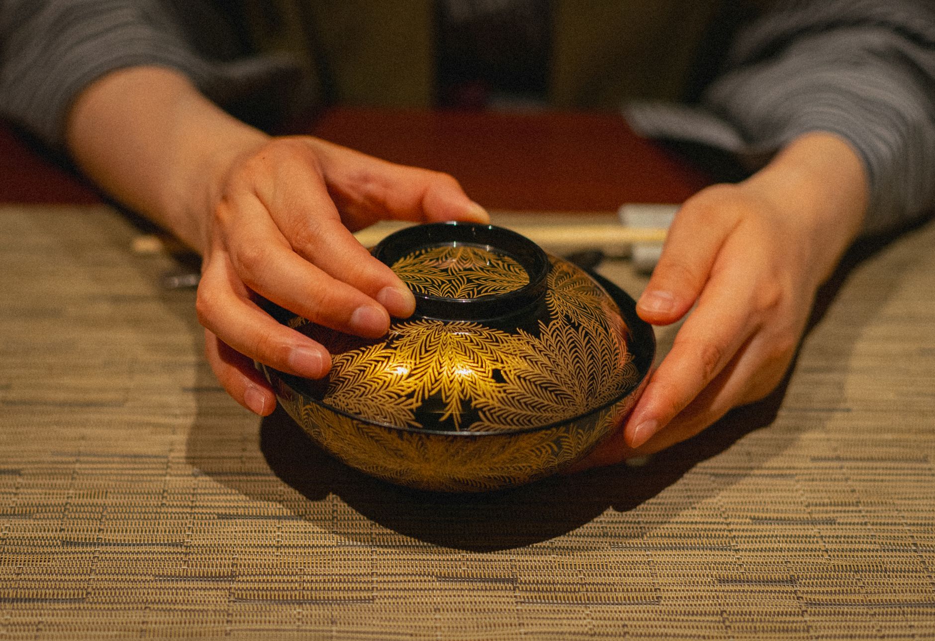 Close-up of hands holding a traditional Japanese lacquerware bowl at a table, capturing dining culture.