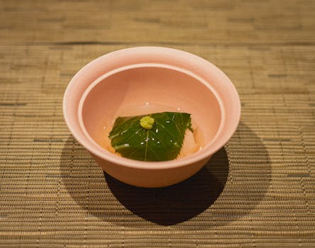 A Japanese gourmet dish garnished with a green leaf and wasabi, served in a pink bowl.