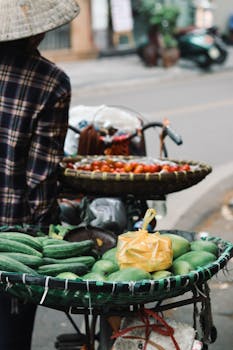 Vibrant street market scene in Hanoi featuring a vendor with fresh cucumbers, tomatoes, and mangoes.