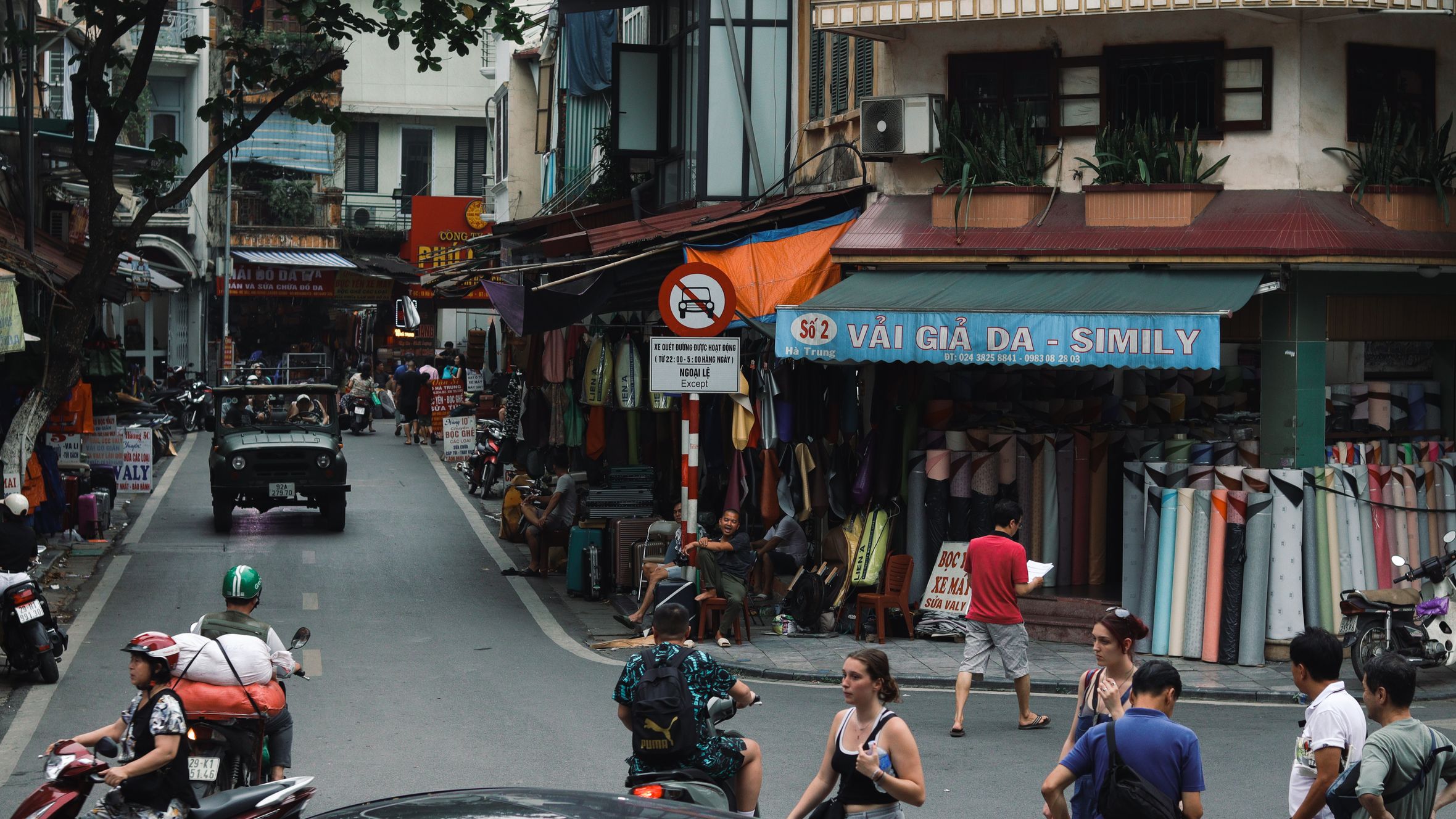 Vibrant street in Hanoi featuring locals shopping, motorbikes, and traditional buildings.