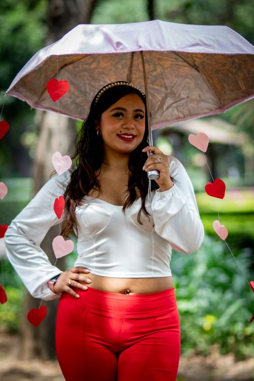Free Smiling woman under an umbrella with hanging hearts, outdoor setting. Stock Photo