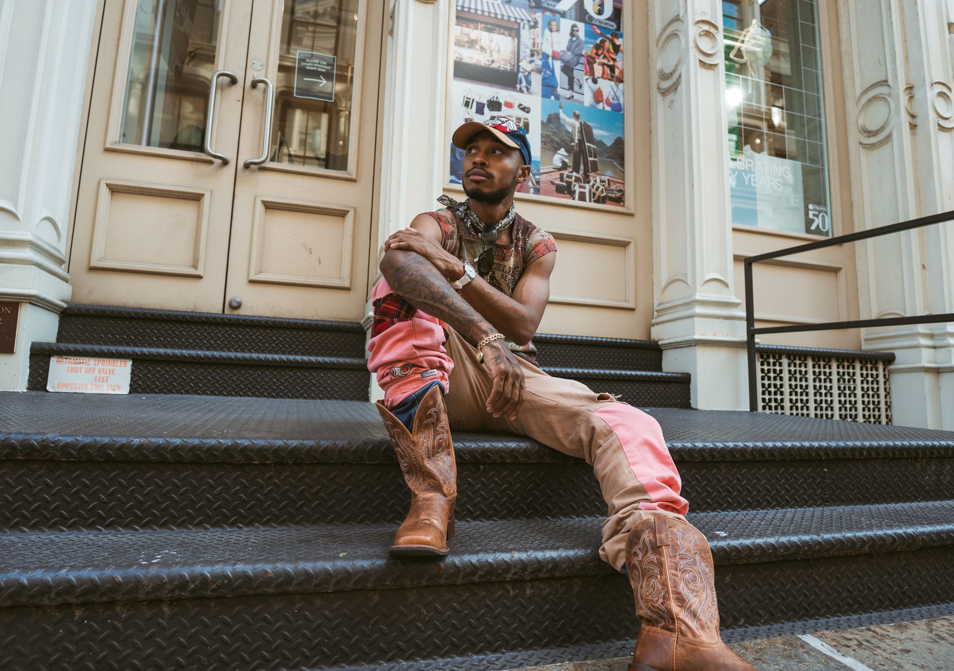 A fashionable man in cowboy boots sits on SoHo steps in New York, capturing urban style.