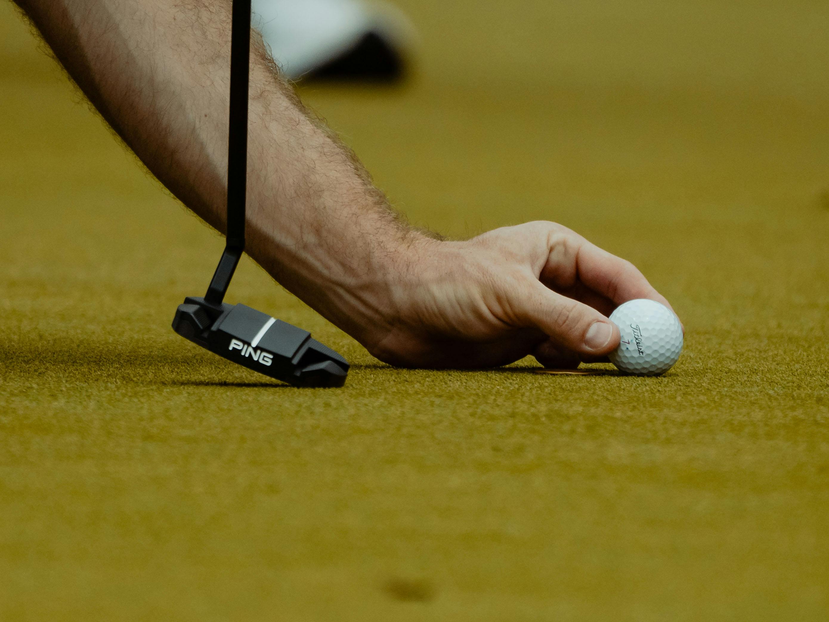 Close-up of a hand placing a golf ball on the green with a putter nearby in Türkiye.