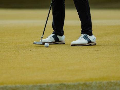 Close-up of golfer's shoes and putter on a golf course green in Türkiye.