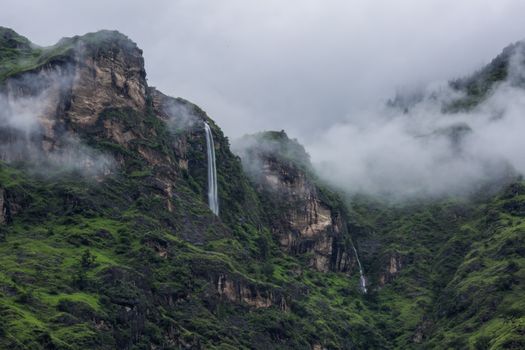 Breathtaking view of a waterfall cascading down misty green mountains in Himachal Pradesh, India.