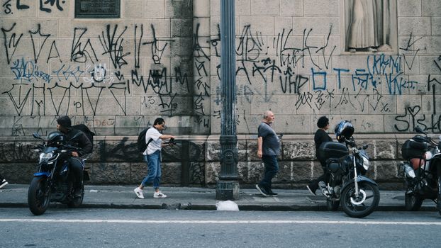 Busy urban street with pedestrians, graffiti, and parked motorcycles.