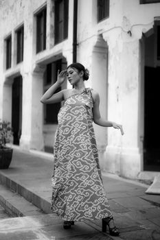 Stylish woman in a patterned gown posing by an old building facade.