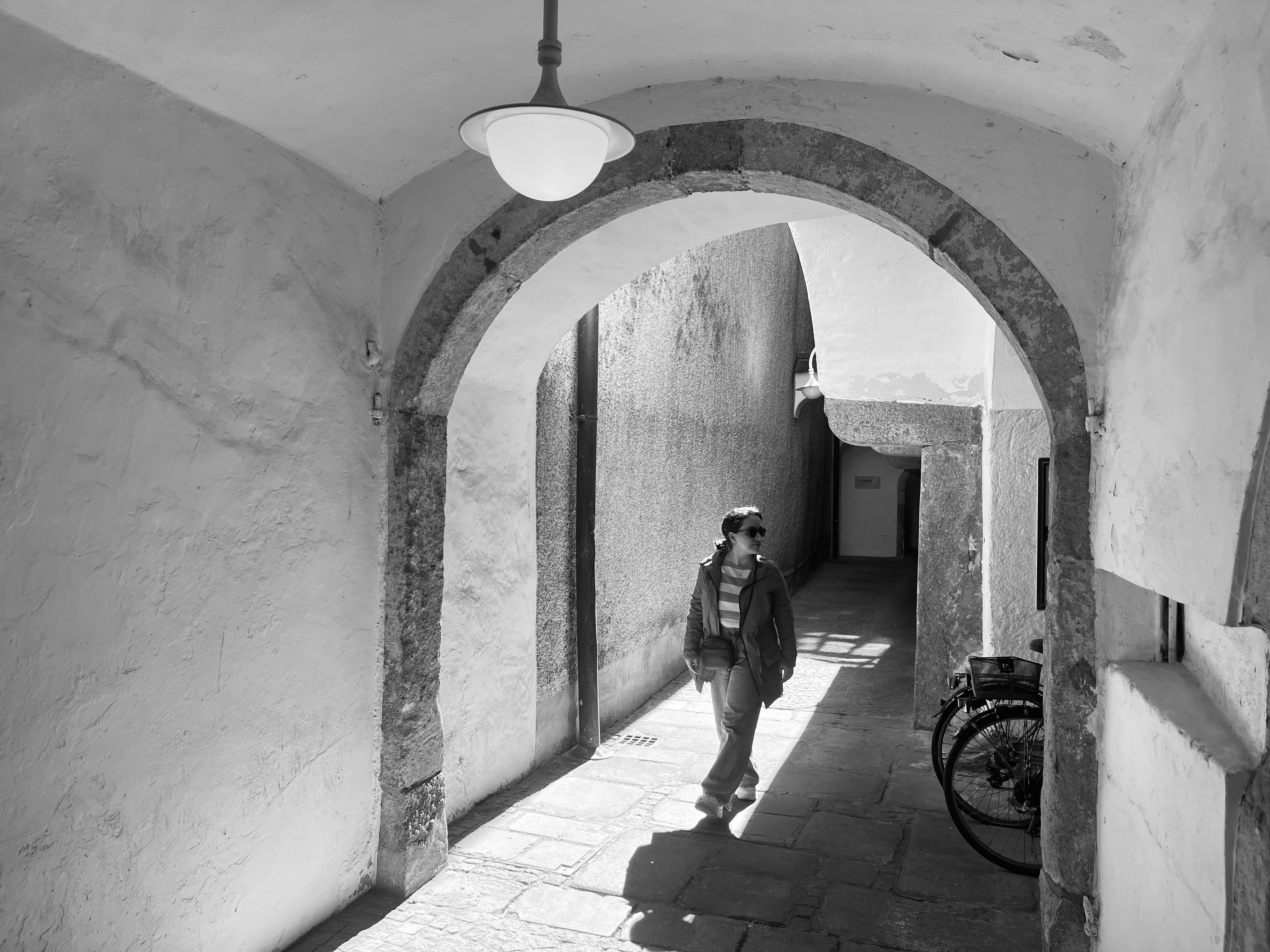 Black and white photo of a person walking in a historic alleyway in Linz, Austria. - Linz