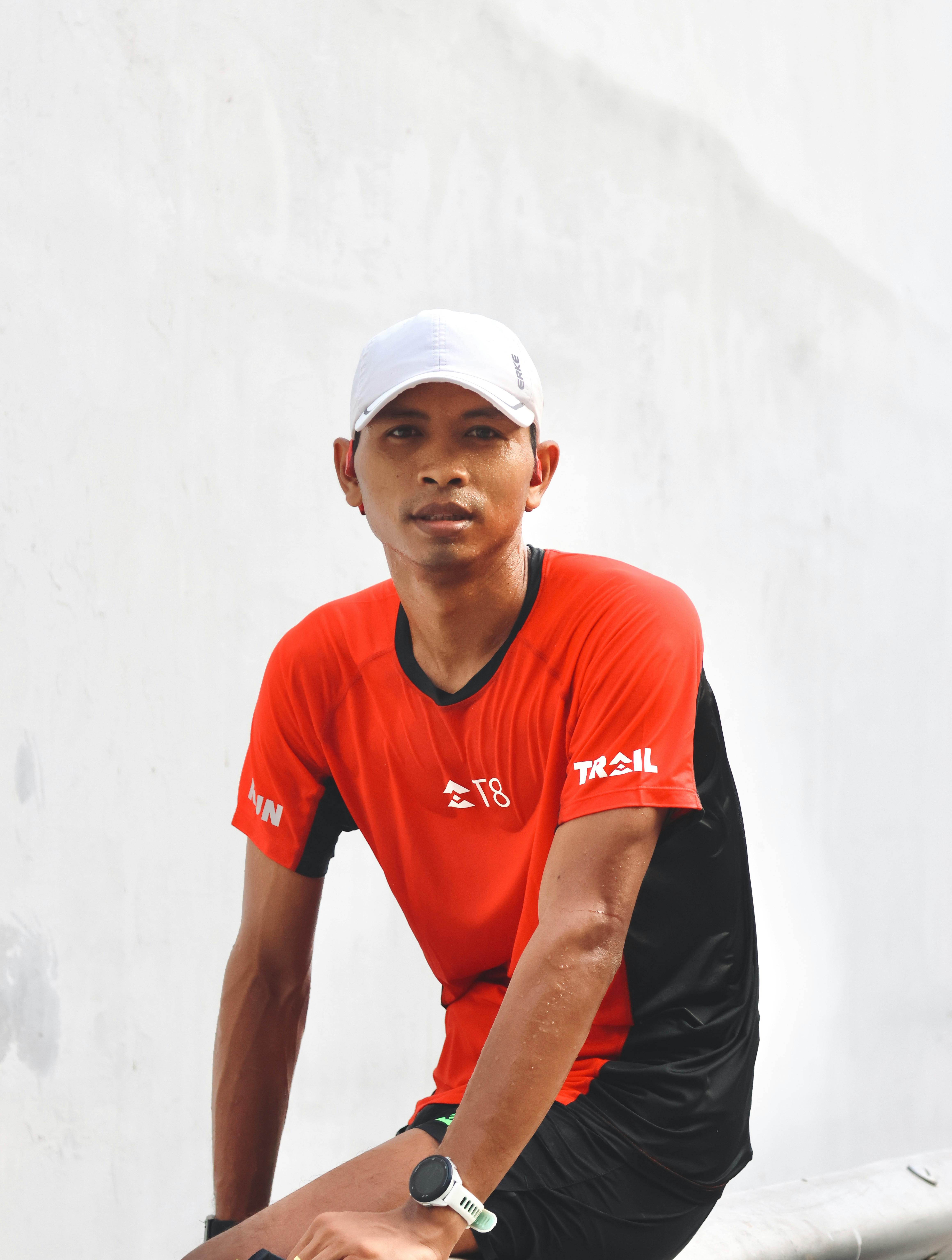 Athlete in red gear resting against a white wall after a run outdoors.