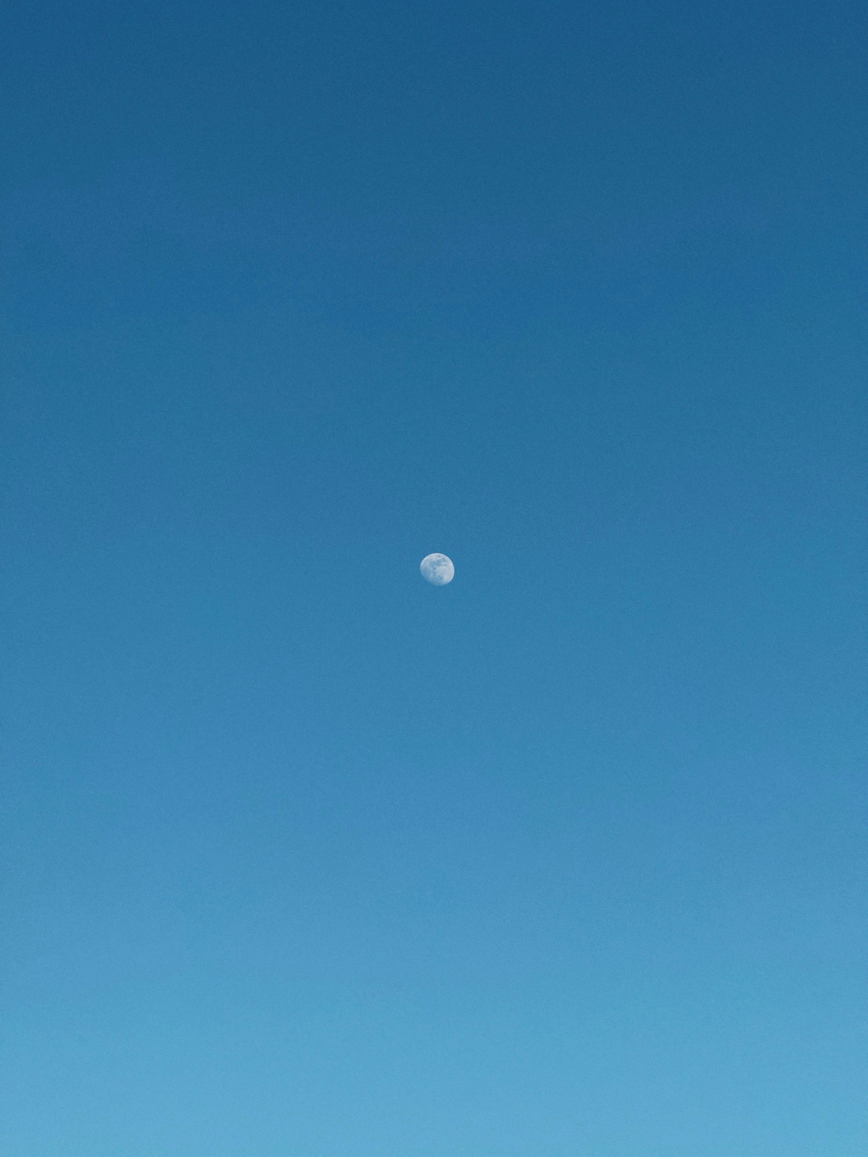 Kostnadsfria En fängslande bild av månen på en ljus, molnfri blå himmel under dagen. Stock foto