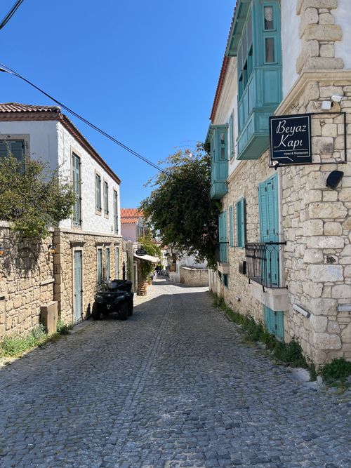 Free Quaint cobblestone street in Alacati, Turkey, with historic stone buildings and vibrant blue shutters. Stock Photo