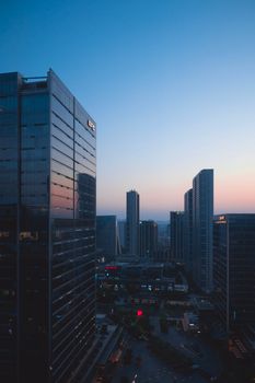 Aerial view of modern city skyline at sunset with high-rise buildings and reflective glass facades.